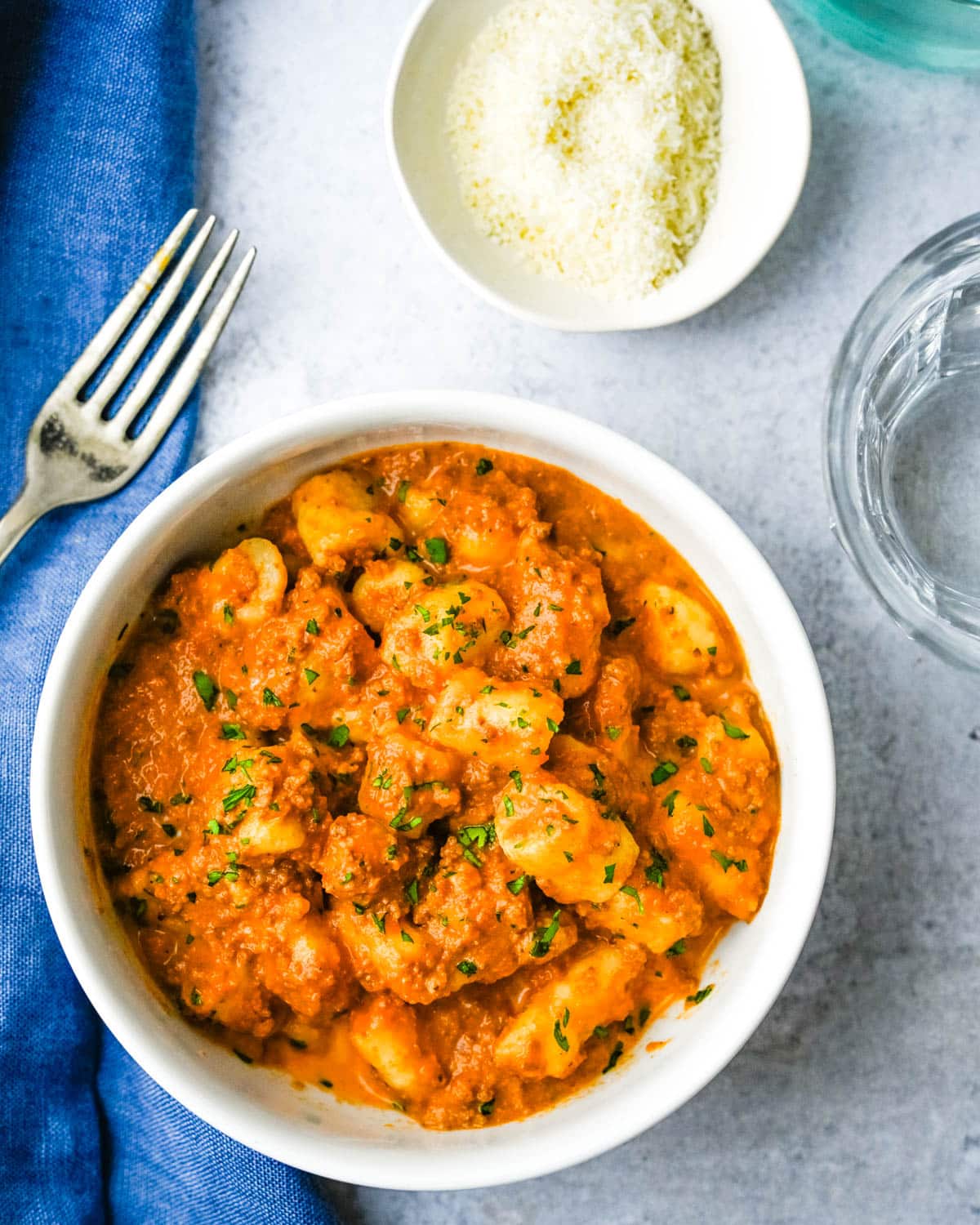 A bowl of creamy gnocchi bolognese with a side dish of parmesan cheese.