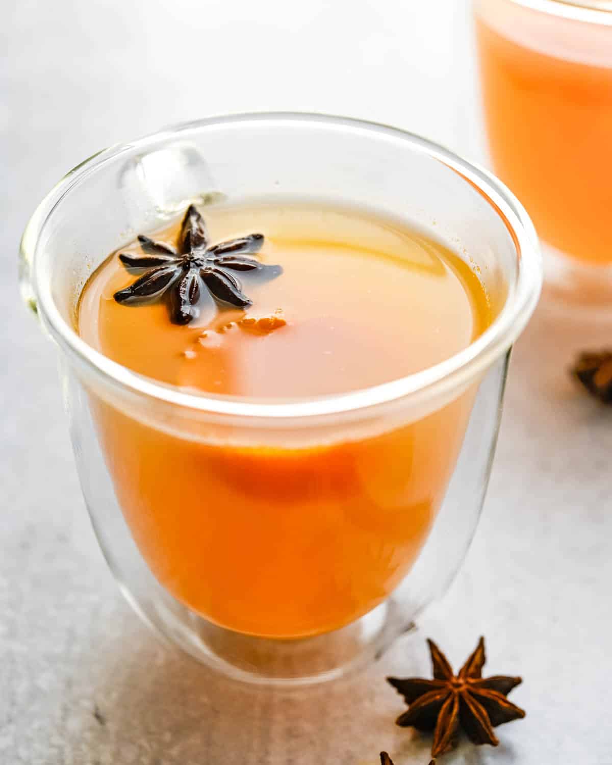 an insulated cup of warm apple cider with a whole star anise floating in it. 