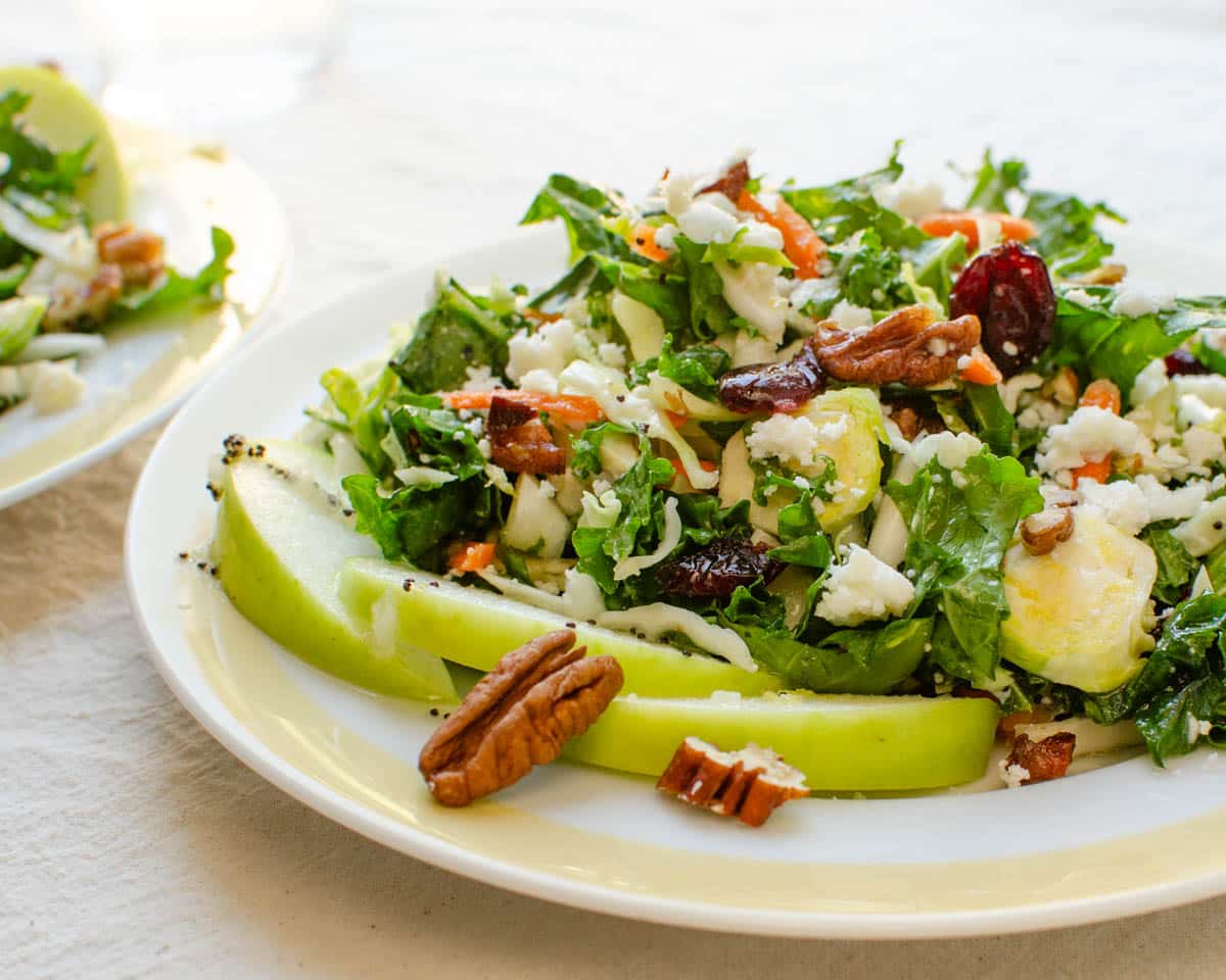 A plate of cabbage and kale salad on a plate with pecans and sliced apples.