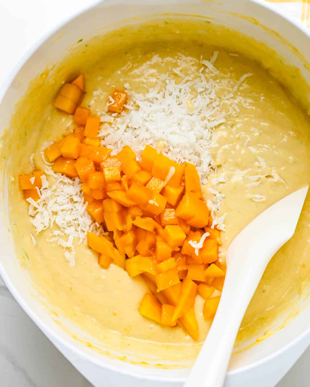 Adding diced mango and flaked coconut to the bread batter. 