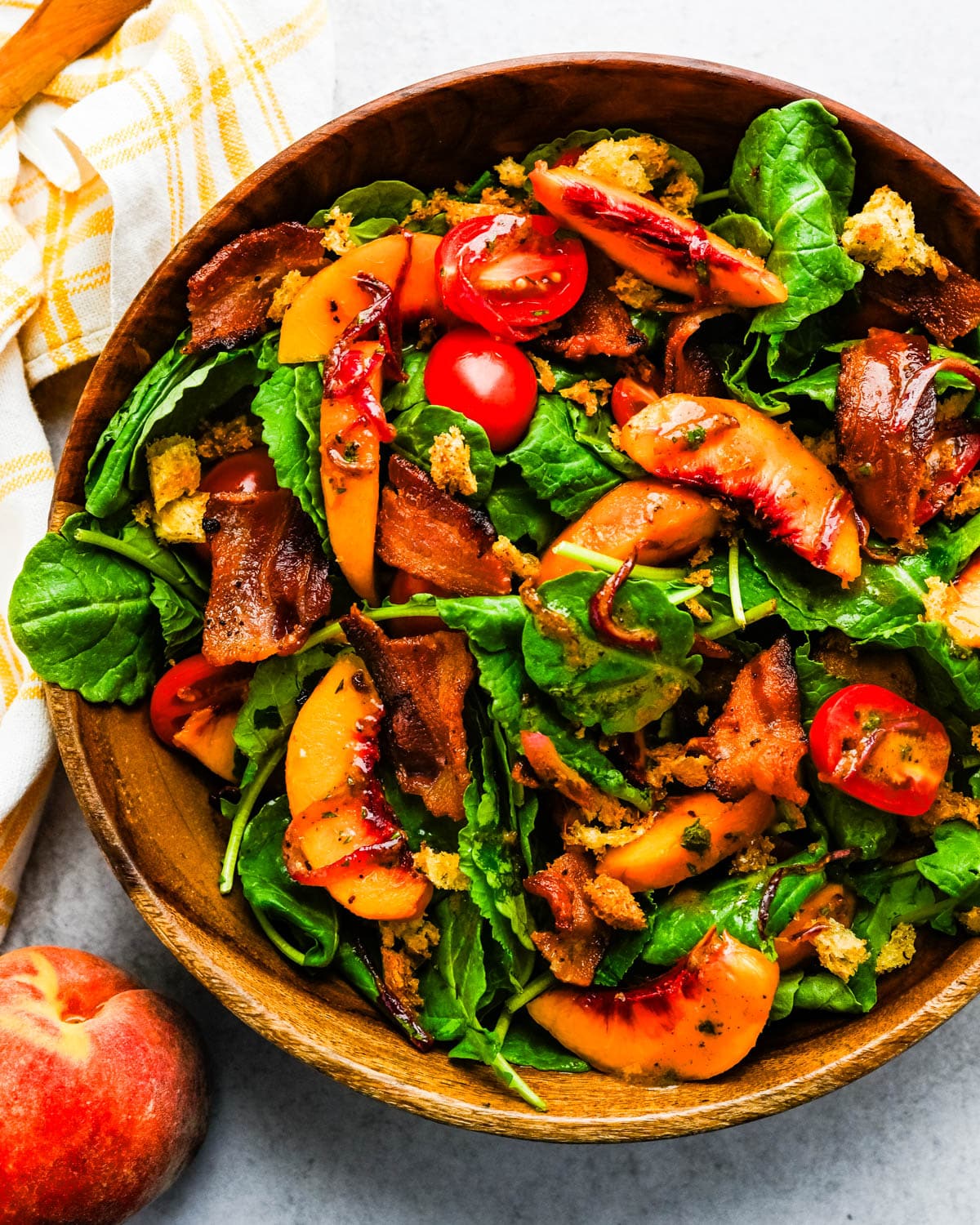 A large bowl of peach bacon and baby kale salad.