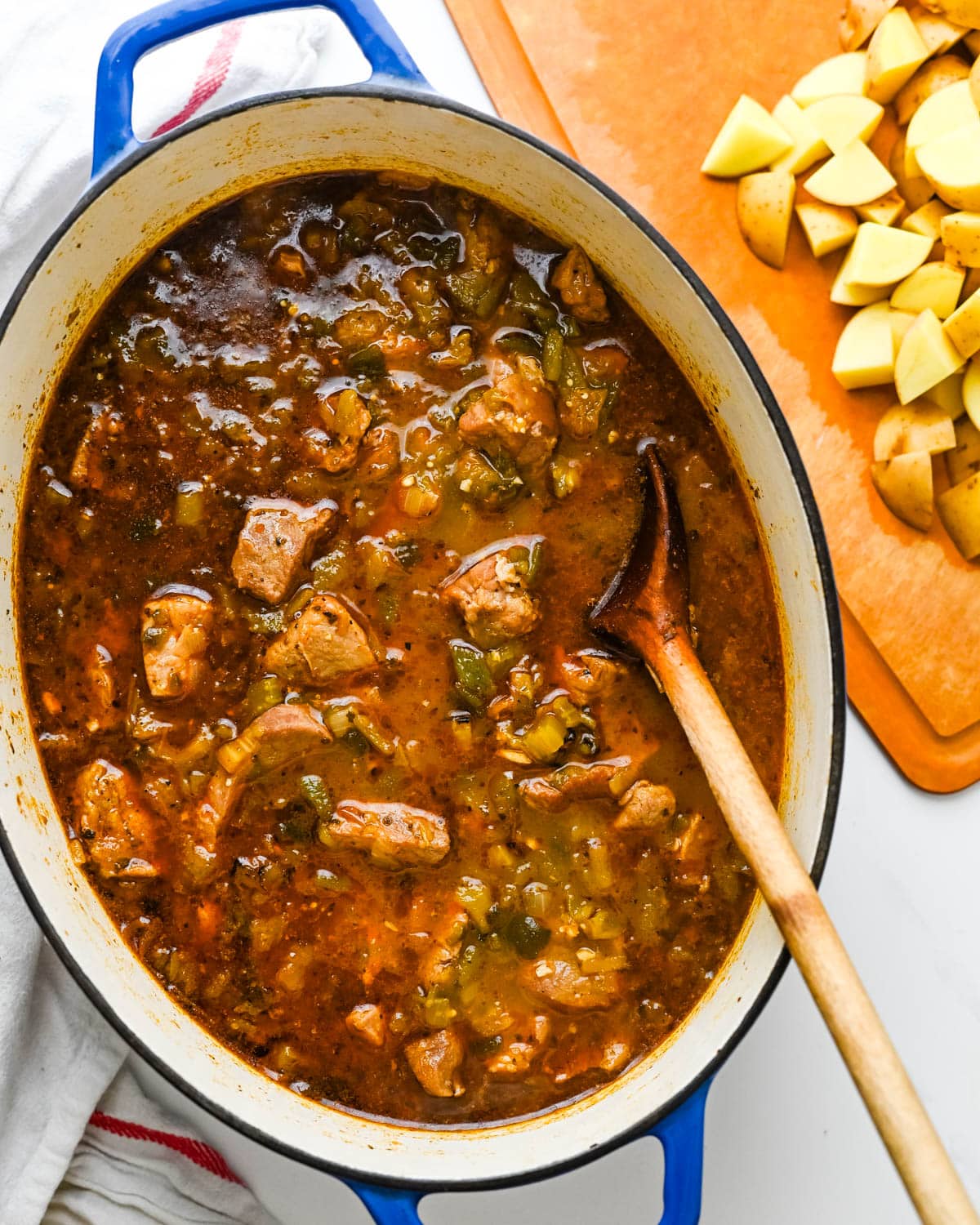 Adding potatoes to the pork stew after it has simmered for one hour.