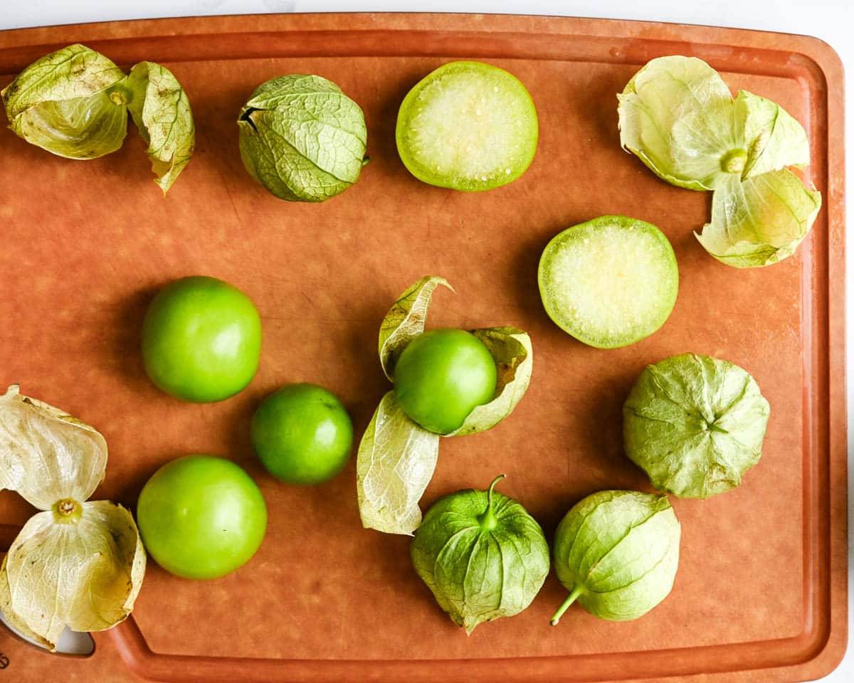 a cutting board with tomatillos being peeled.