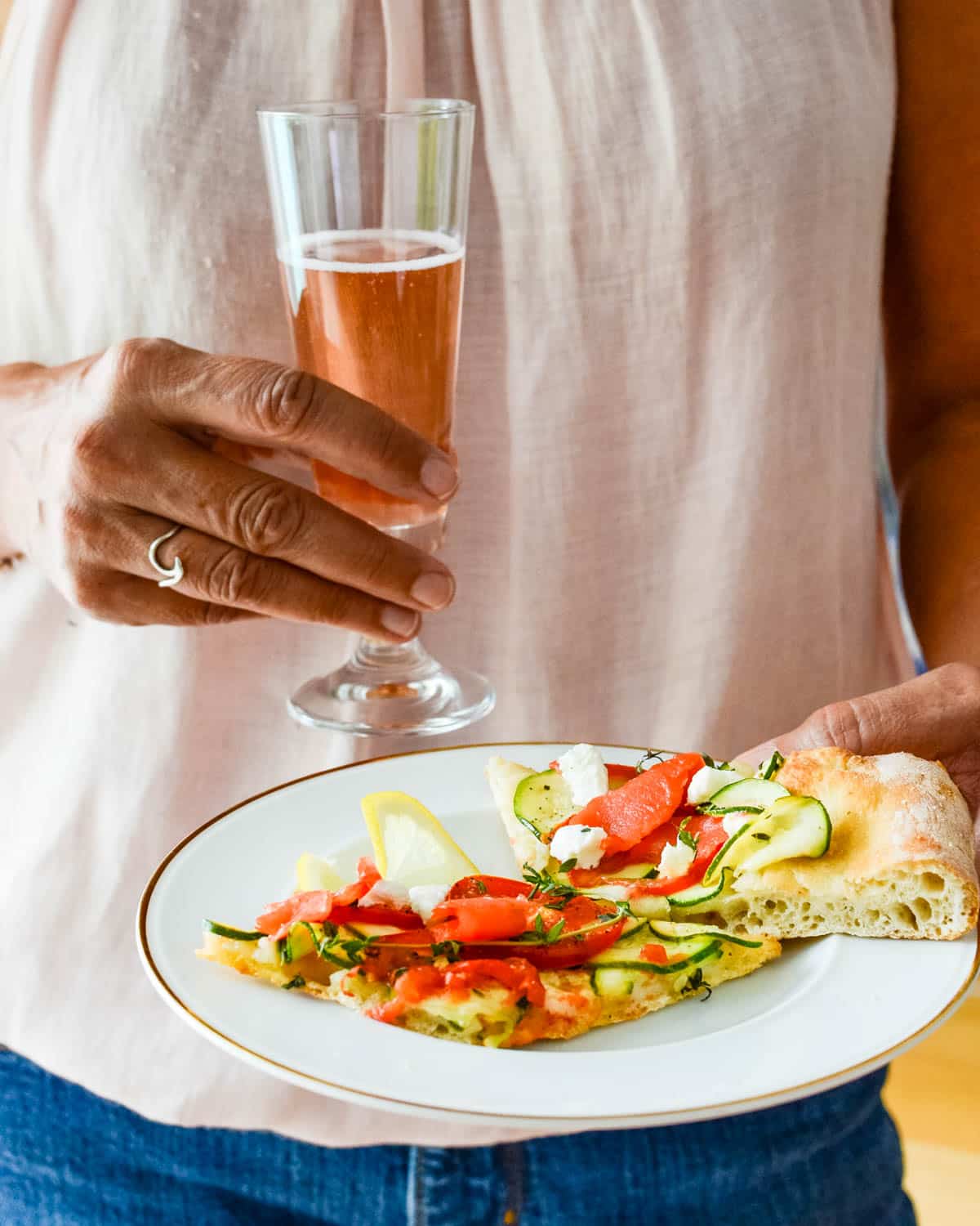 Holding a plate of smoked salmon pizzas with a glass of sparkling rosé.