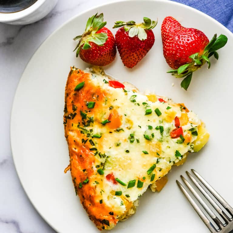 A slice of crustless veggie quiche on a plate with strawberries.