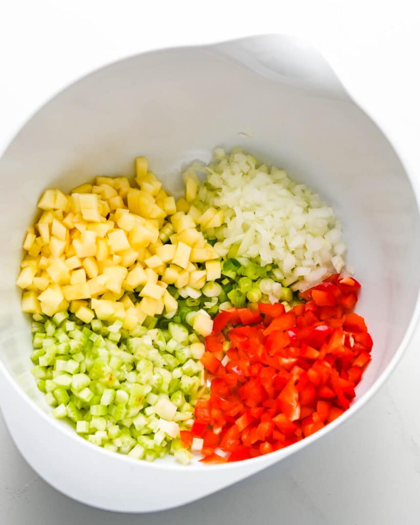 Diced celery, bell peppers, scallions, onion and apples in a bowl. 