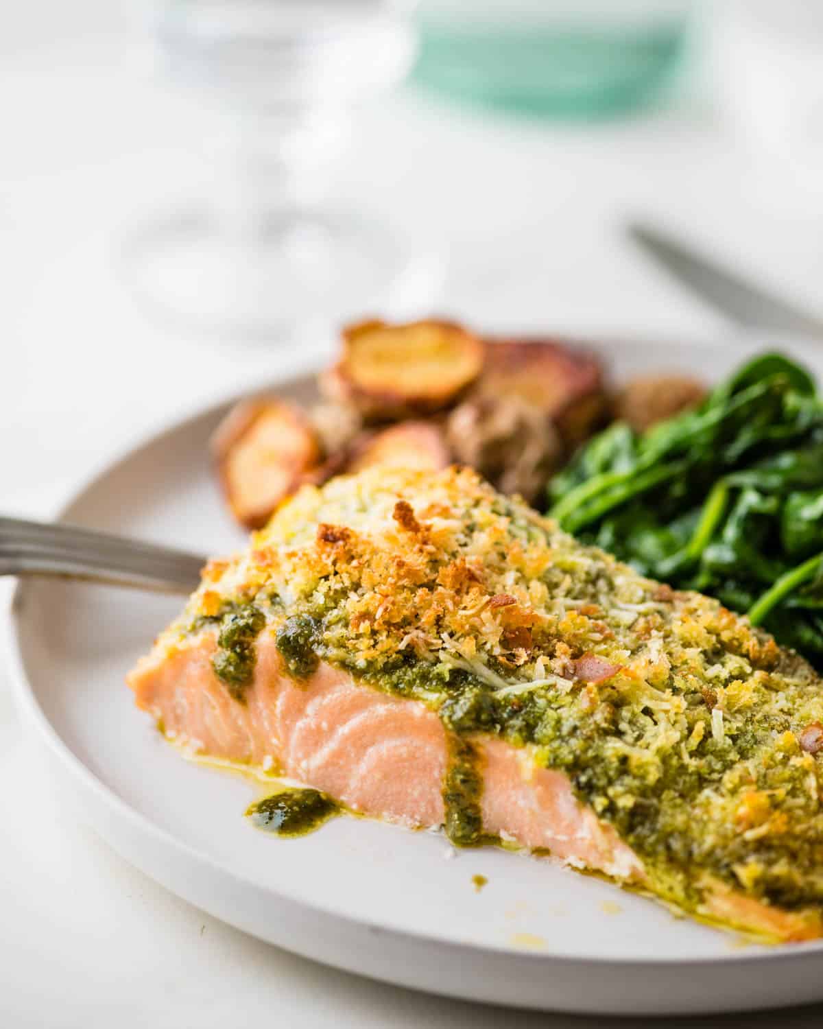 Serving the baked salmon with pesto sauce on a plate with spinach and roasted potatoes. 