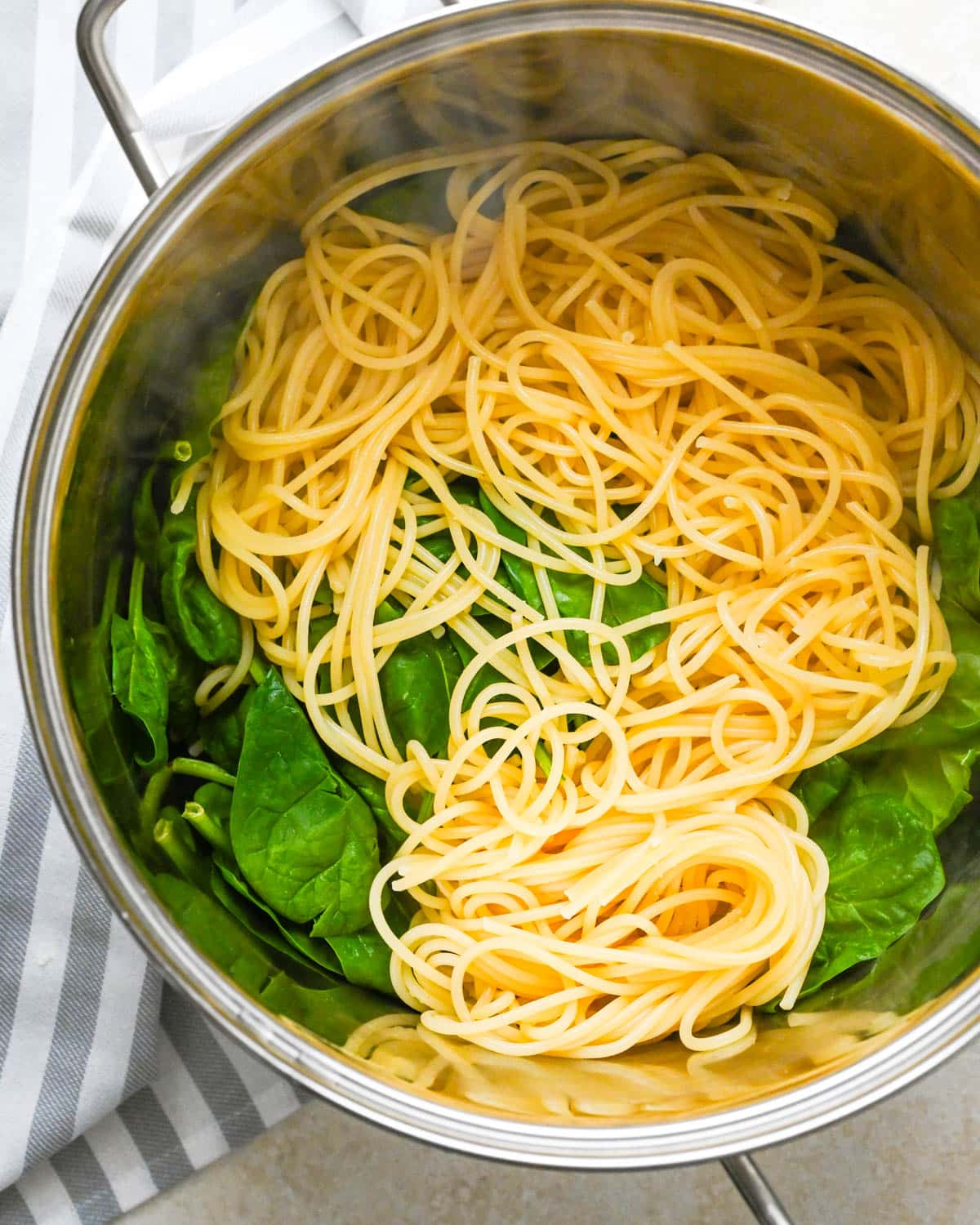 Tossing cooked spaghetti with fresh spinach to wilt it.