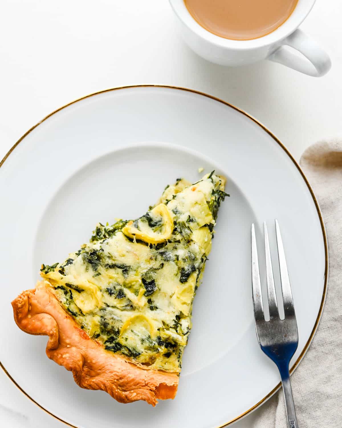 Serving a slice of spinach artichoke quiche with a cup of coffee for brunch.
