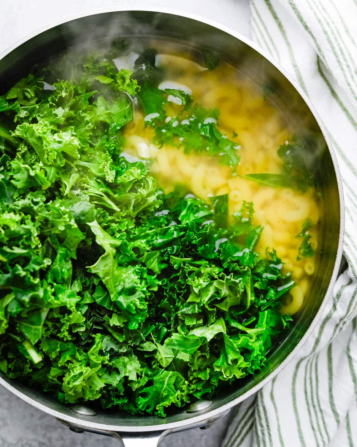Blanching fresh kale leaves with the cooked macaroni noodles.