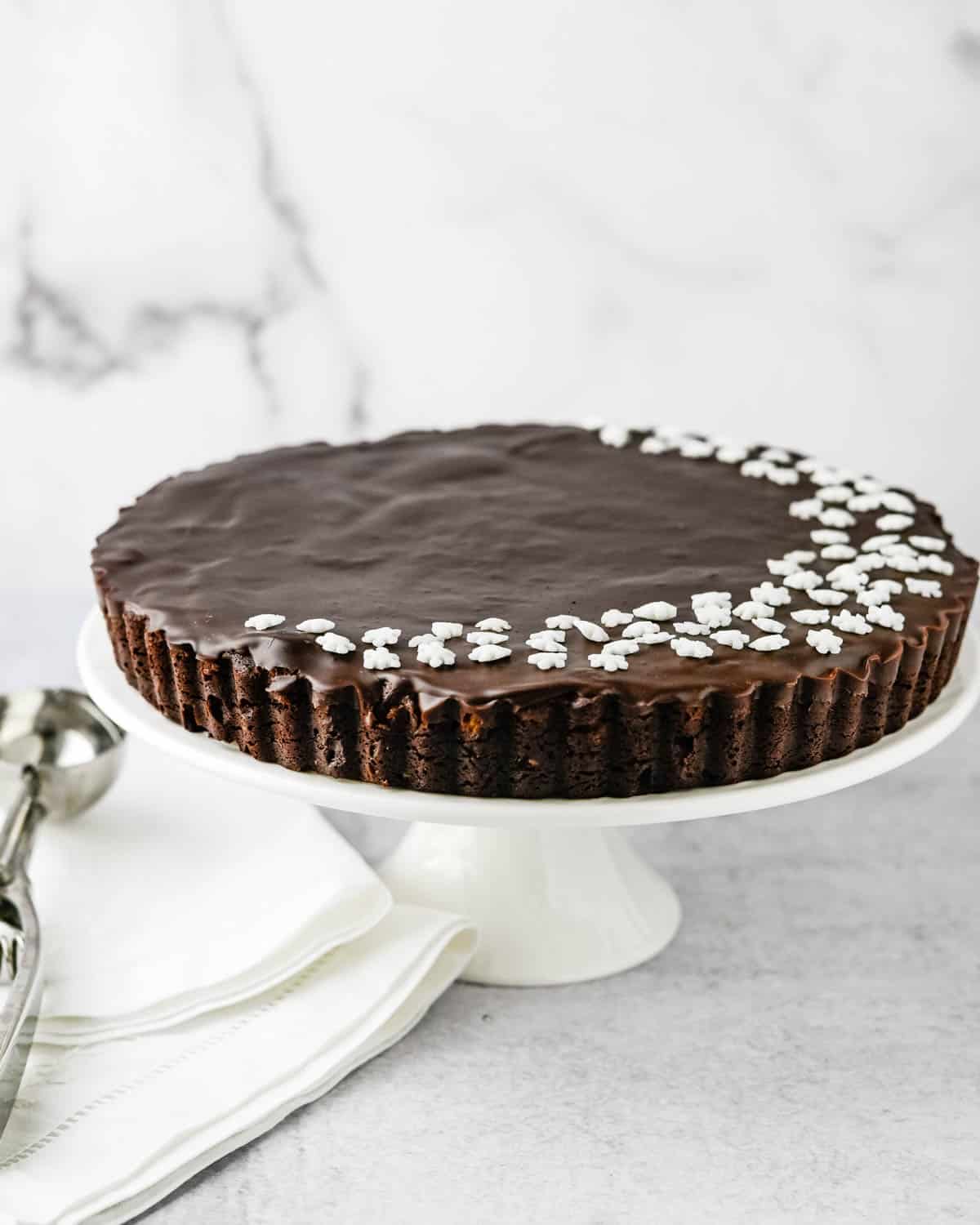 The decorated chocolate fudge tart on a cake plate. 