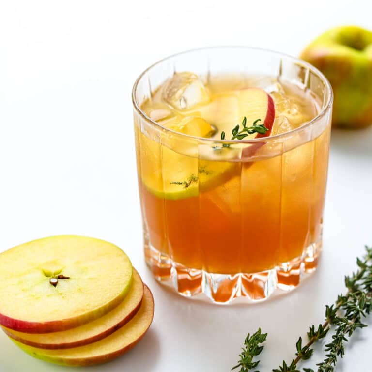 Serving the apple cider cocktail with a slice of apple and fresh thyme sprig.
