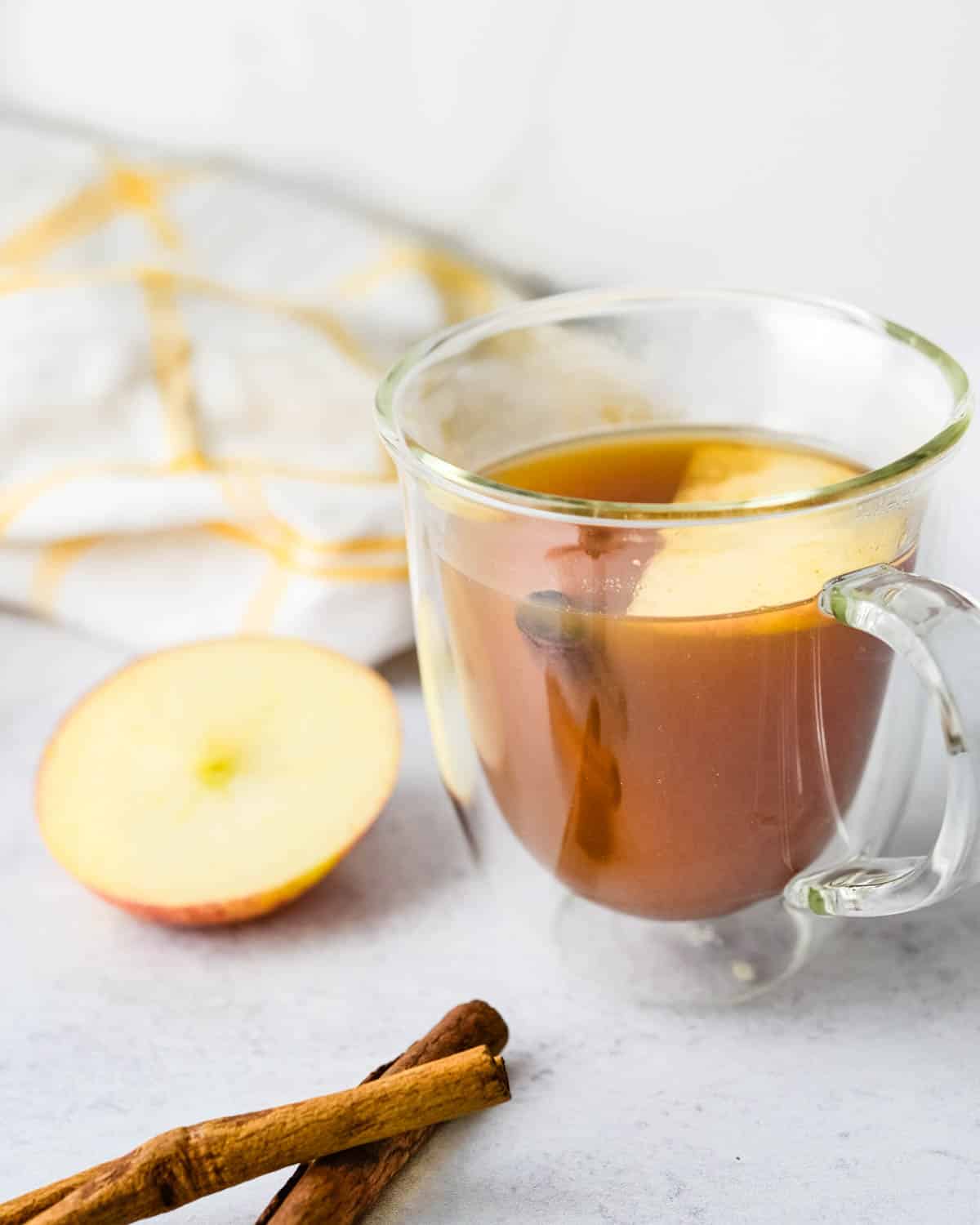 A cup of hot cider tea with a cinnamon stick and apple slice.