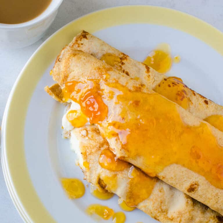 Cutting into a plate of breakfast crepes with ricotta and apricot jam.