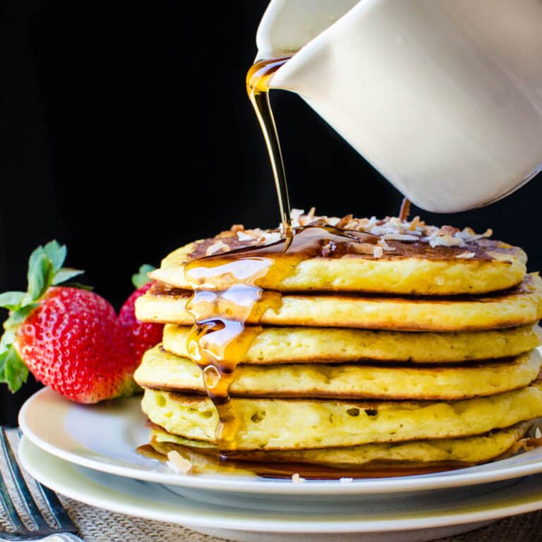 Pouring syrup over a stack of the orange coconut pancakes.