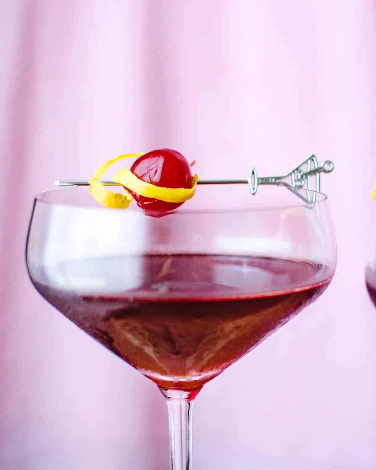 A crimson kiss Valentine's Cocktail in a coupe glass with a cherry garnish
