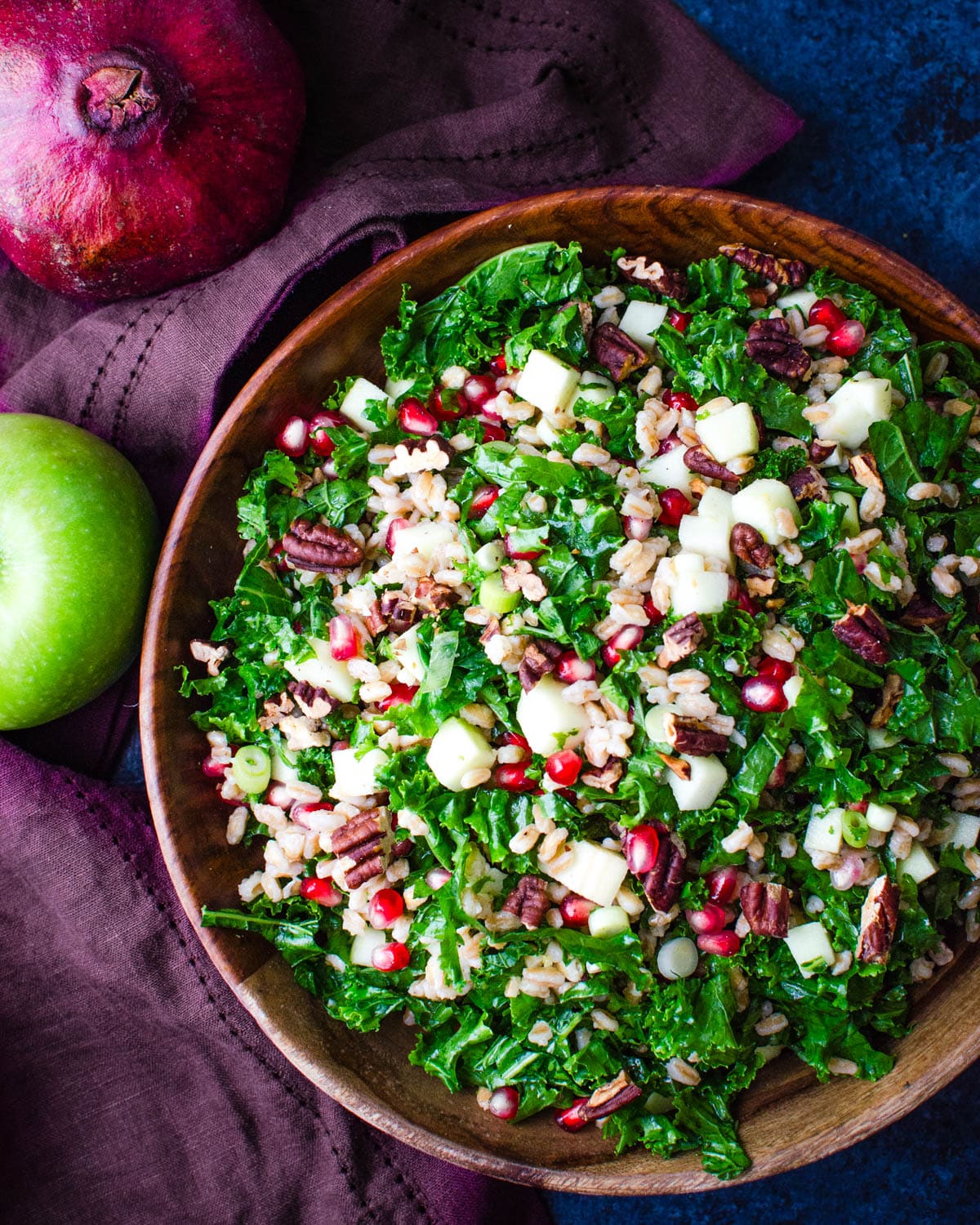 Kale pomegranate salad with apples and pecans in a wooden serving bowl.
