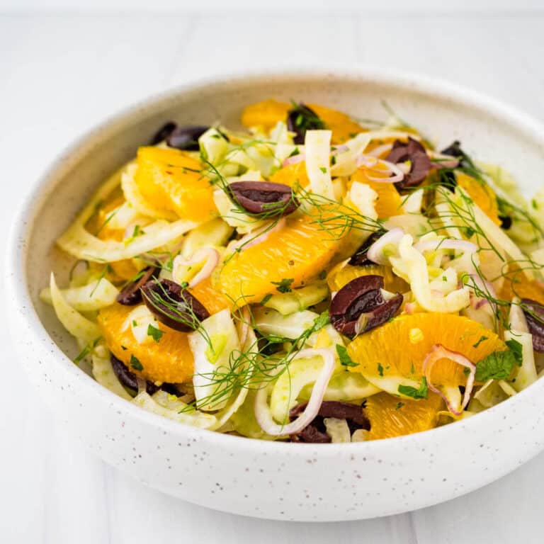 An orange fennel salad with kalamata olives in a white serving bowl.