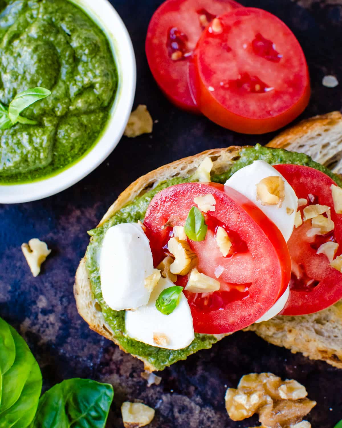 Slathering walnut pesto over grilled toasts and garnishing with cheese and tomato.