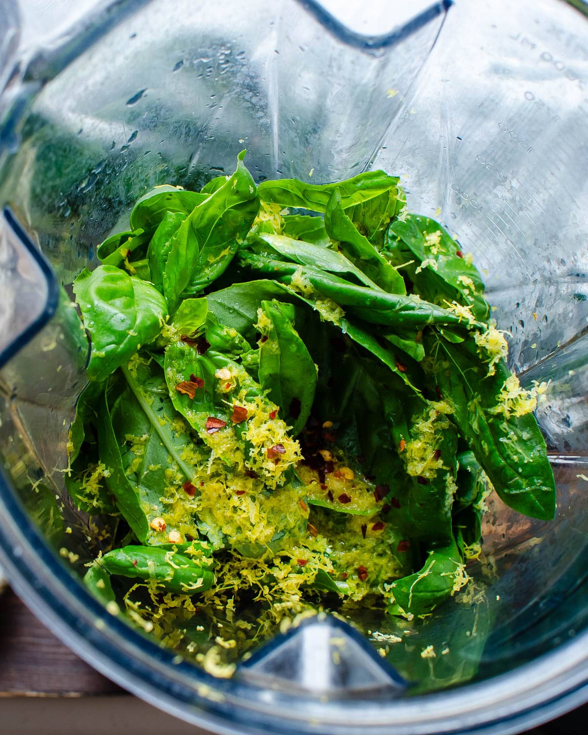 Adding lemon zest and red pepper flakes to the basil in a blender. 