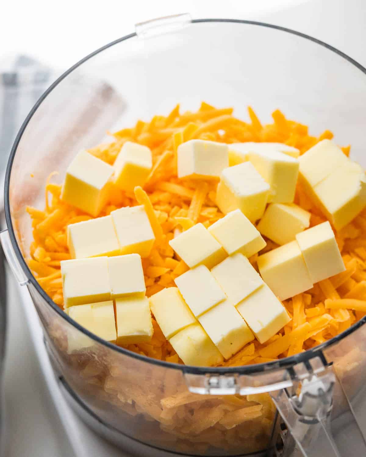 Combining shredded cheddar cheese and diced butter in a food processor.