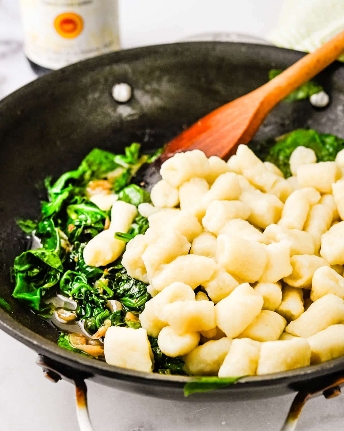 Tossing cooked gnocchi with the spinach.
