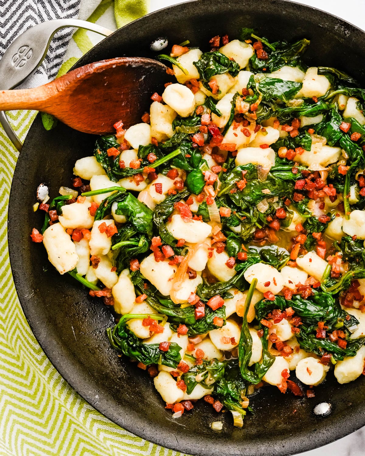 Adding pancetta to the Italian gnocchi and spinach to serve.