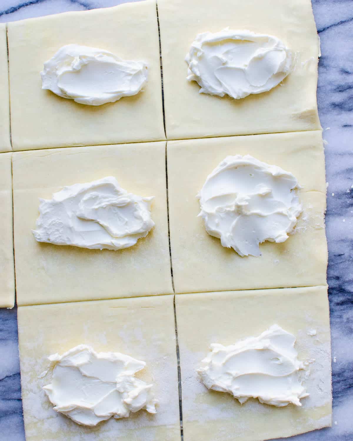 Smearing cream cheese filling into the middle of each square of puff pastry.
