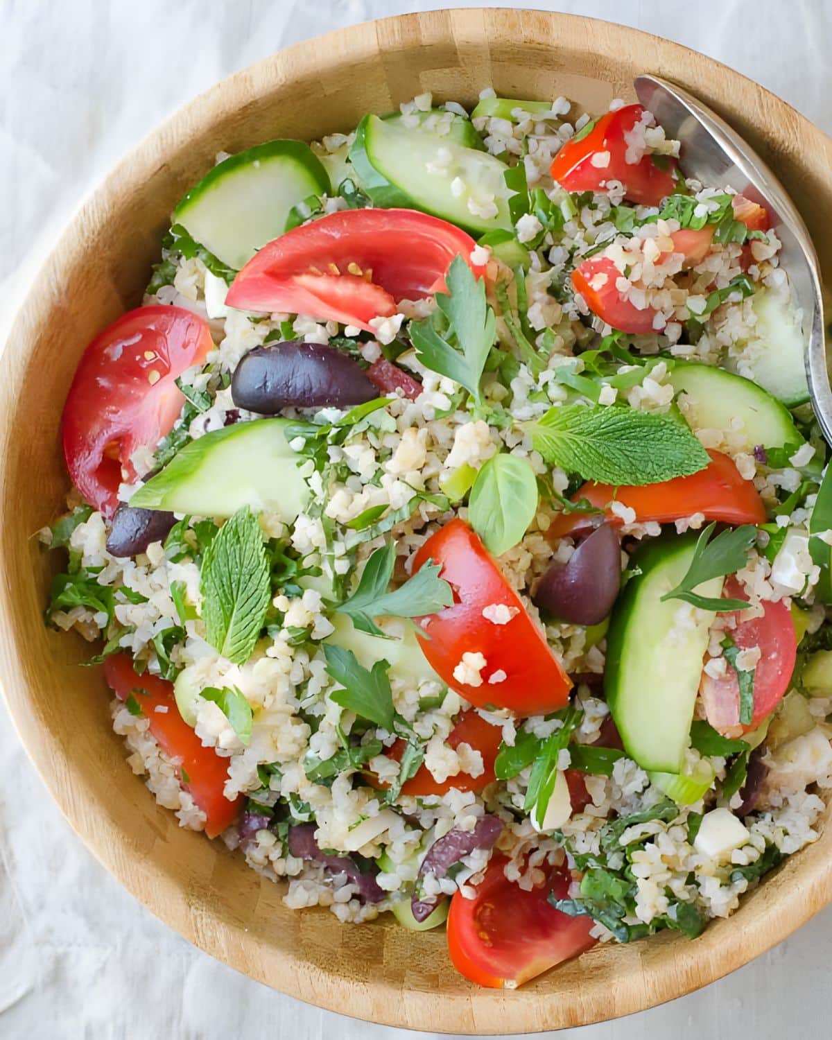A bowl of tabbouleh with tomatoes, cucumbers and kalamata olives.