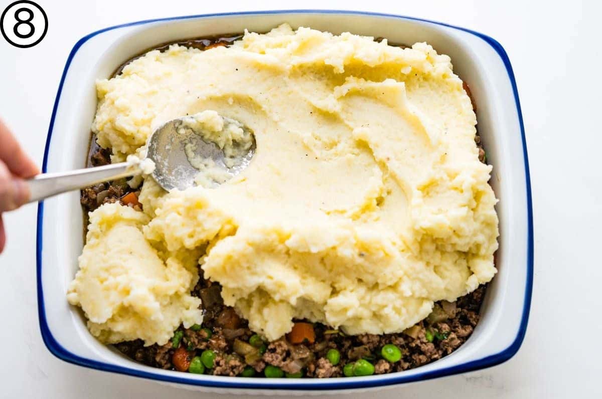 spreading mashed potatoes over the ground lamb.