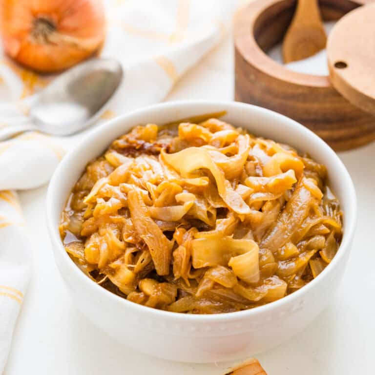 A white bowl of caramelized onions with a spoon on the side.