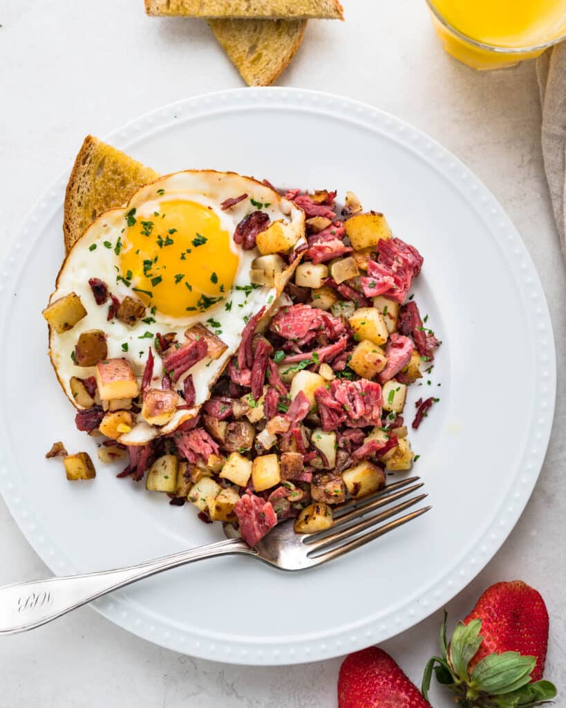 A plate of homemade corned beef hash with eggs and toast.