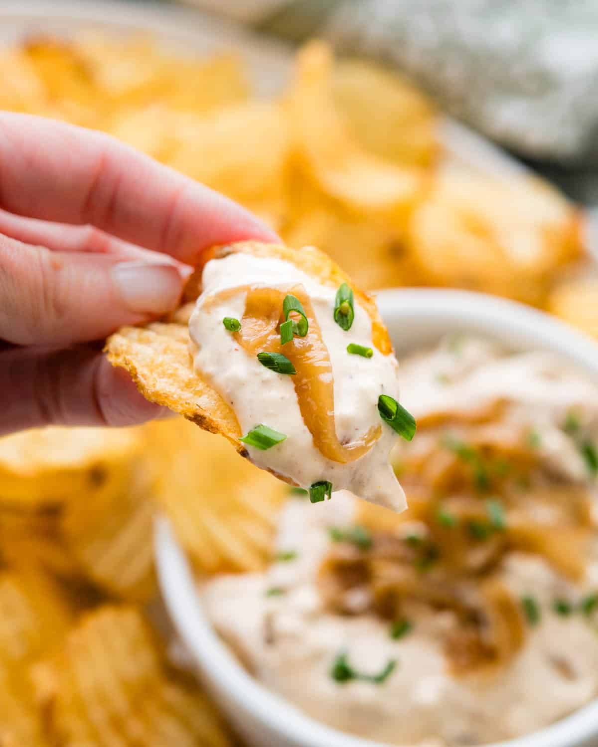 Holding a potato chip with sour cream and onion dip and a caramelized onion.