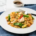 a white plate filled with shrimp and chicken fried rice with Prik Nam Plaom the side.