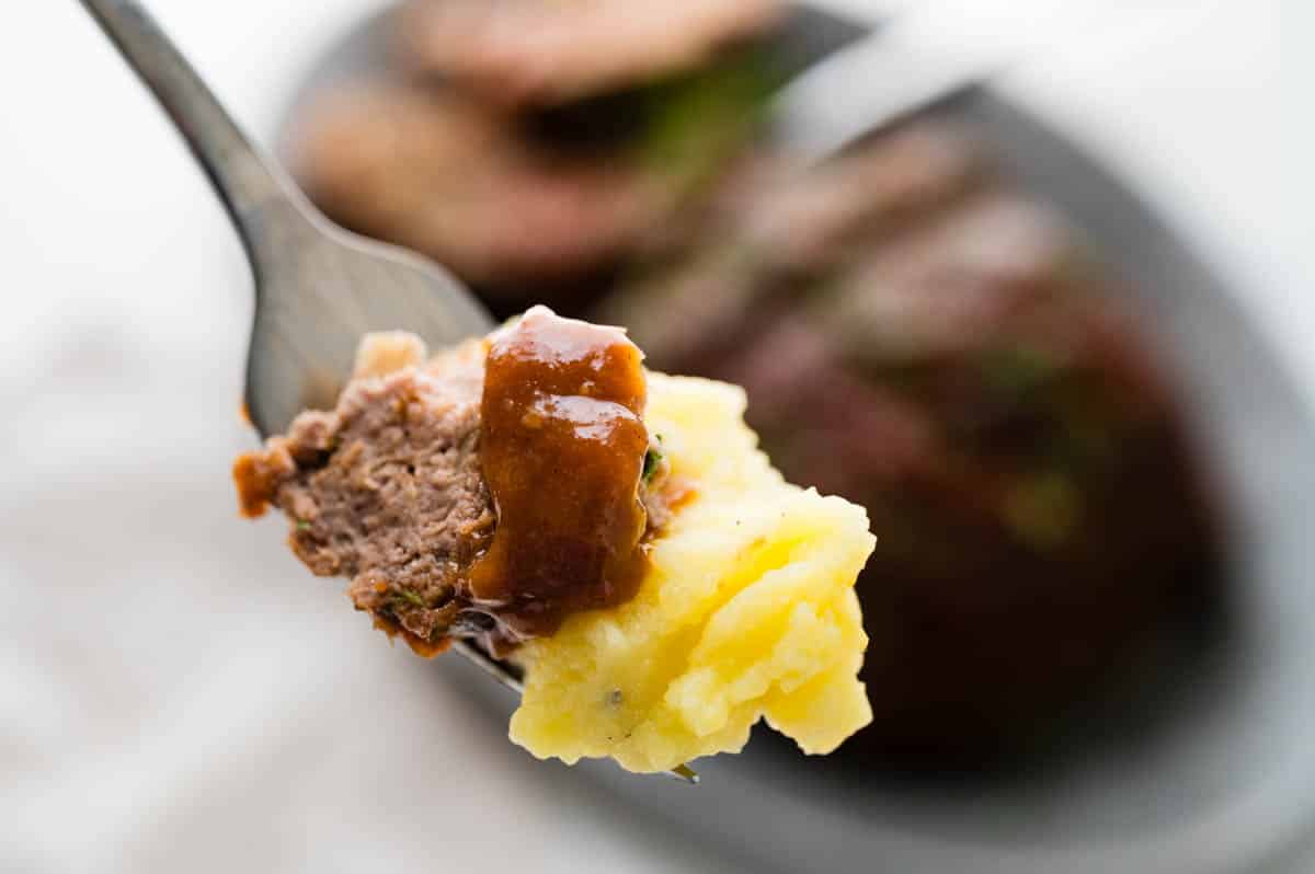 Taking a bite of meatloaf with extra glaze and mashed potatoes.