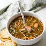 Serving a bowl of the lentil bean soup with ham in a white bowl.