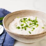 A stoneware bowl of horseradish sauce garnished with minced chives.