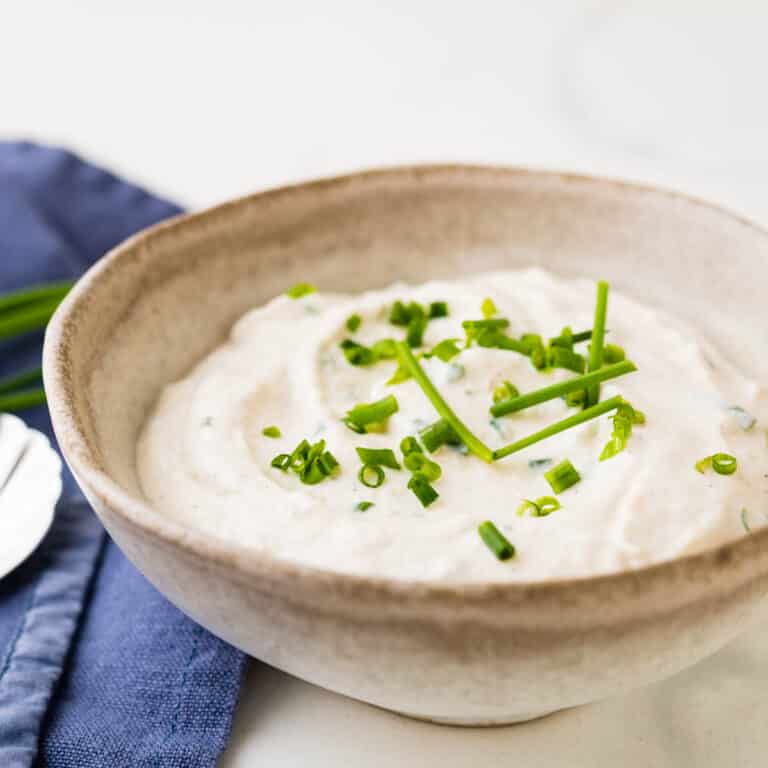 A stoneware bowl of horseradish sauce garnished with minced chives.