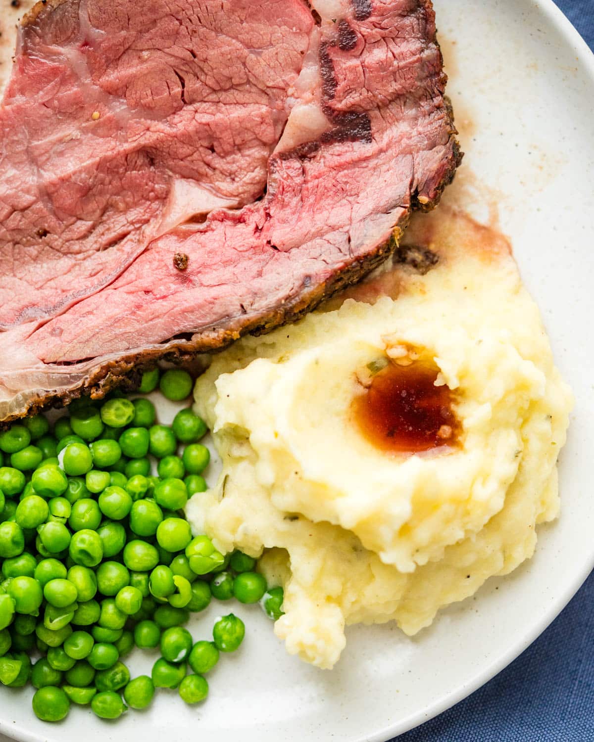 A plate of prime rib with mashed potatoes and peas.