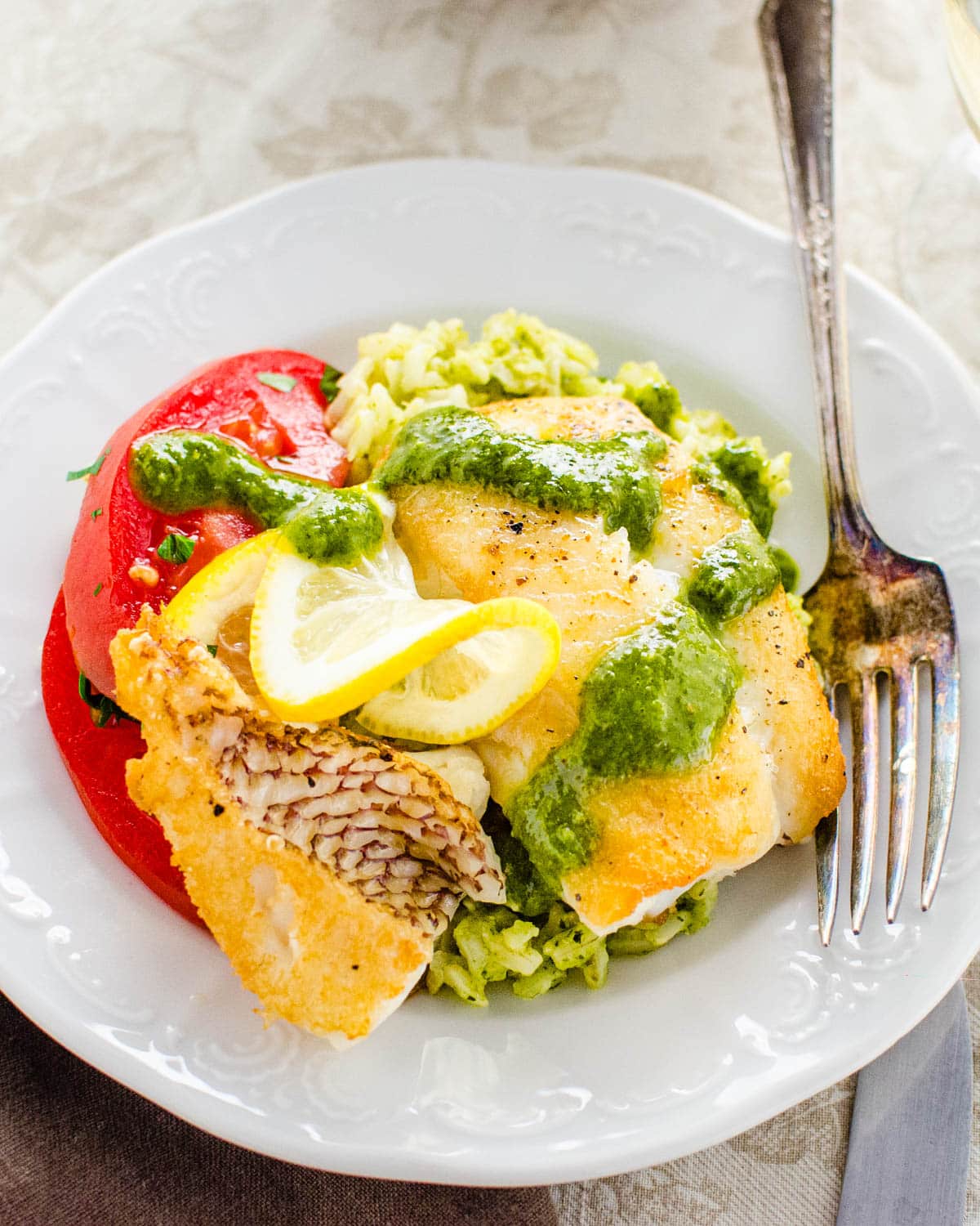 A golden piece of snapper with green sauce and lemon wedge.