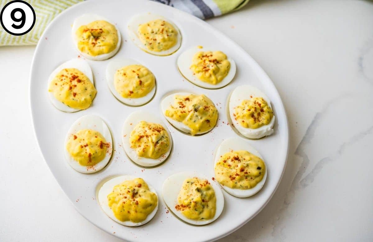 Garnishing the dill pickle deviled eggs with paprika.
