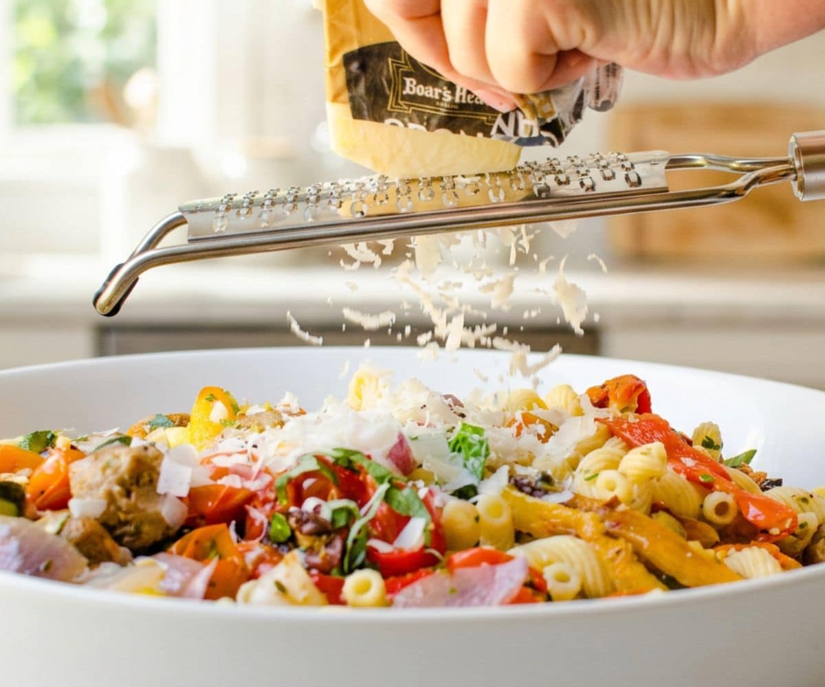 shaving parmesan cheese over the pasta with peppers onions and sausage.