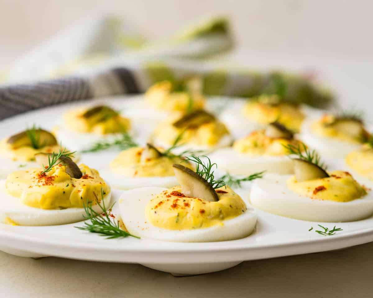 A tray of deviled eggs with pickles and dill.