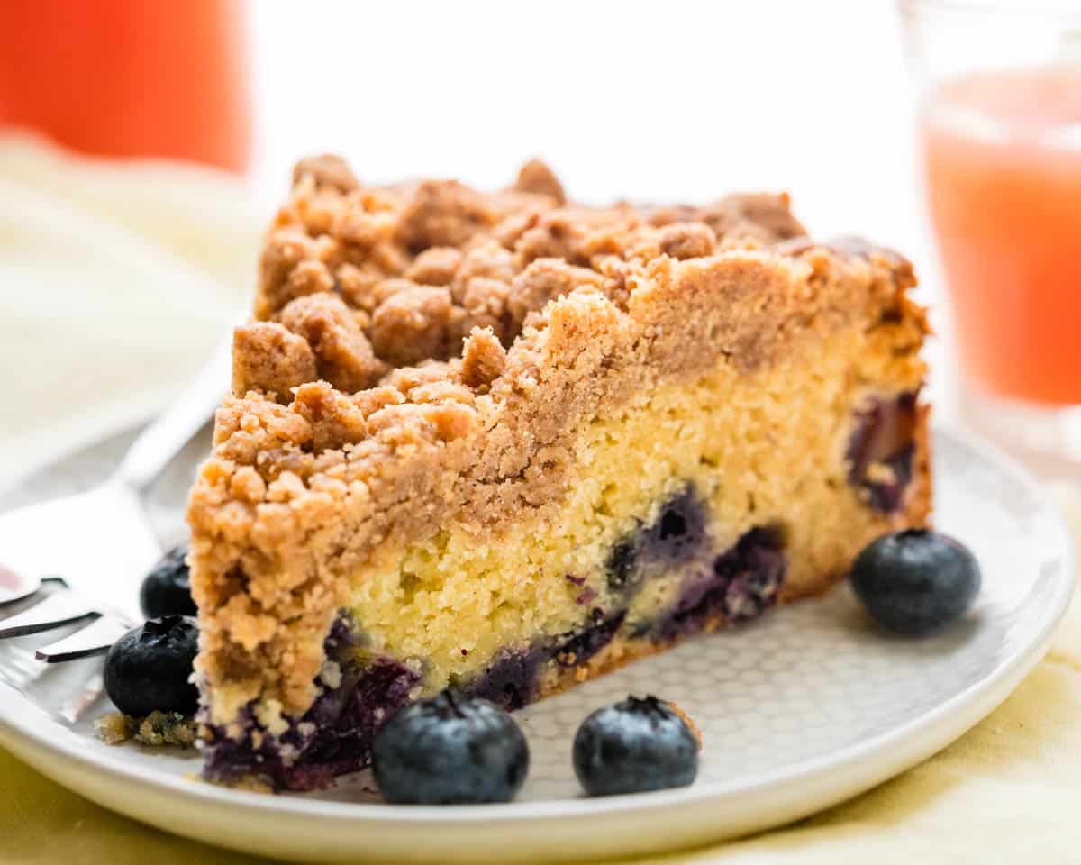 Blueberry sour cream coffee cake with streusel topping on a white plate with extra blueberries.