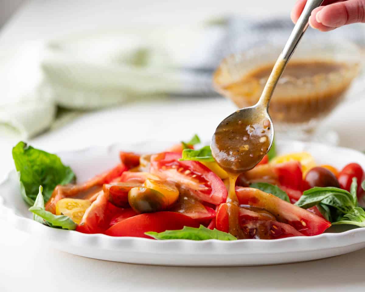 Drizzling balsamic dressing vinaigrette over a tomato salad.