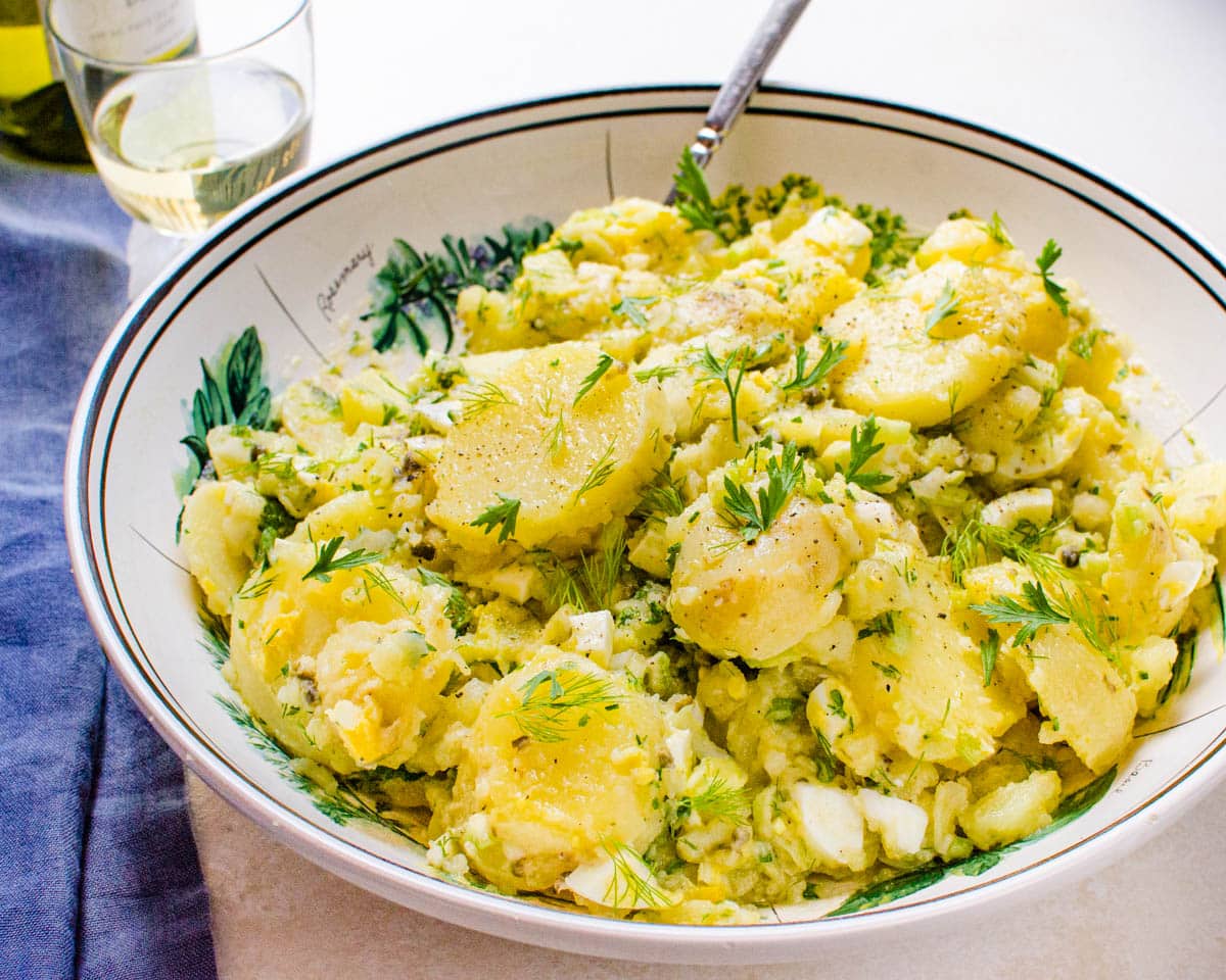A bowl of the potato salad (no mayo) with a spoon in it.