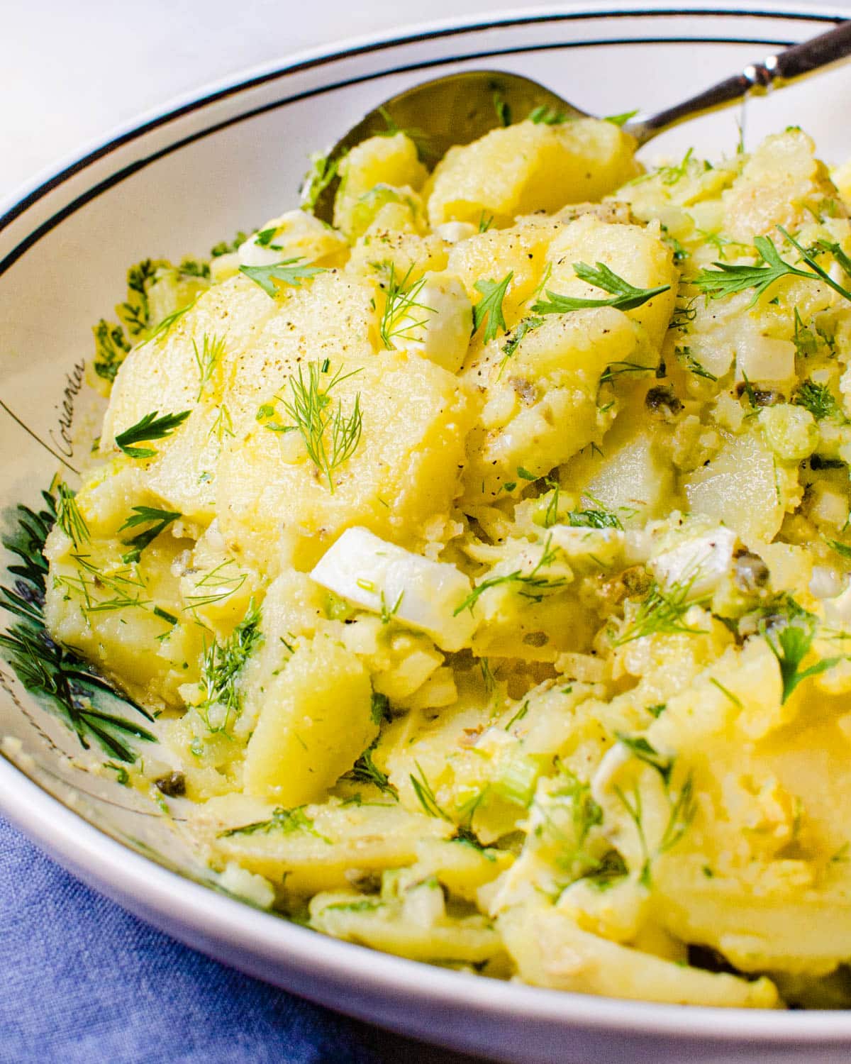 A closeup shot of the French potato salad in a bowl with a serving spoon.