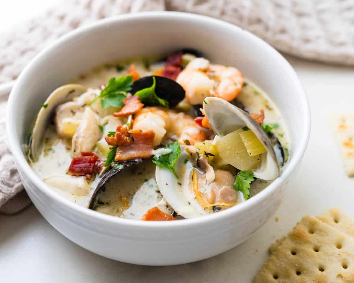 Fish and seafood chowder served in a white bowl with saltines.
