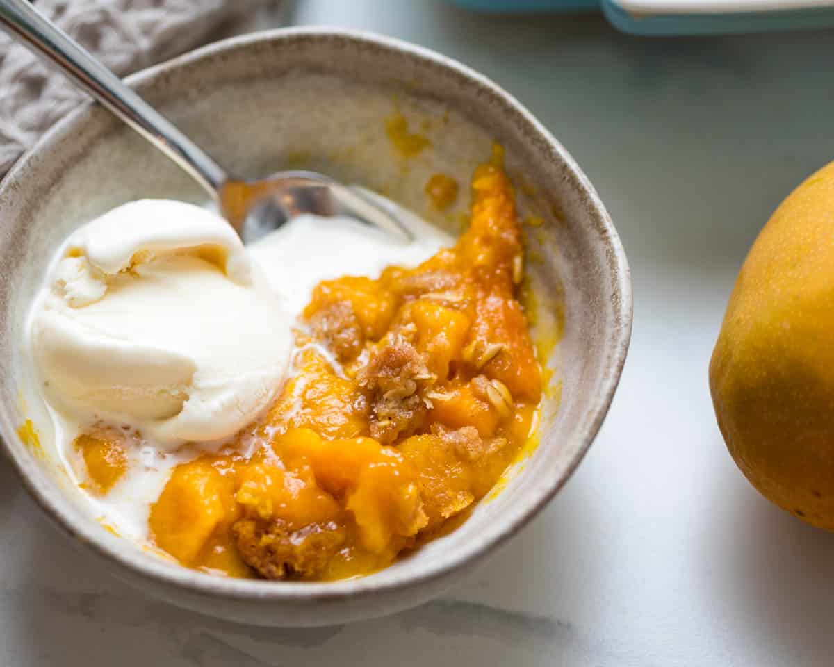 A bowl of mango crisp with ice cream melting into it.