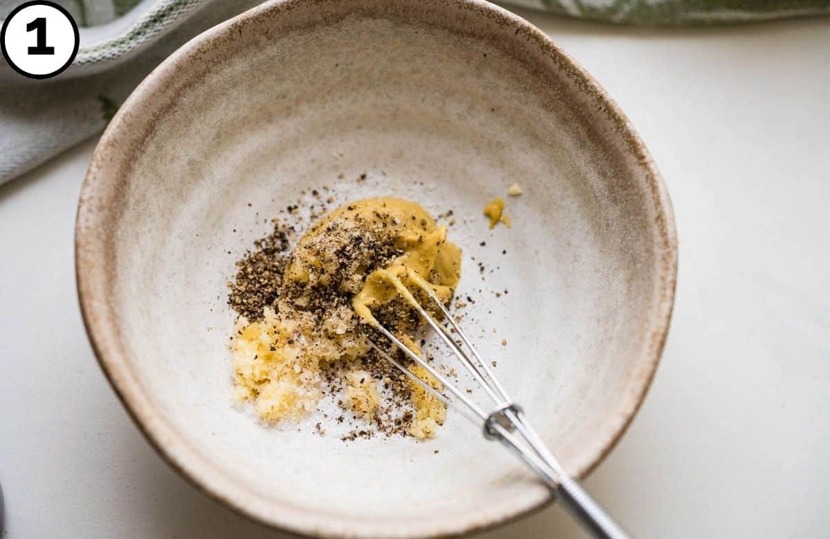 Mixing the Dijon, garlic, salt and pepper in a stoneware bowl.